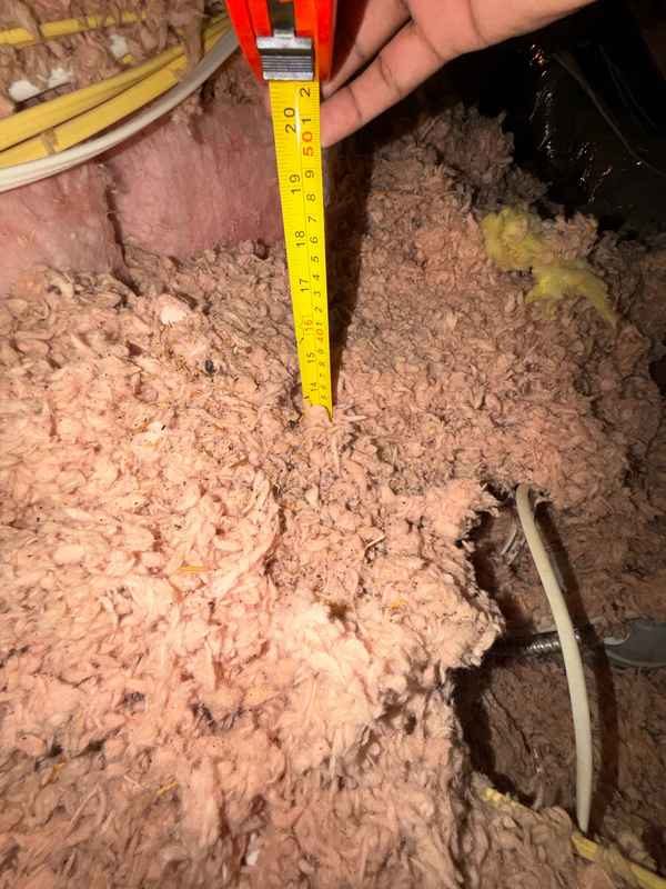 Inspector midiendo la profundidad del aislamiento del ático con una regla