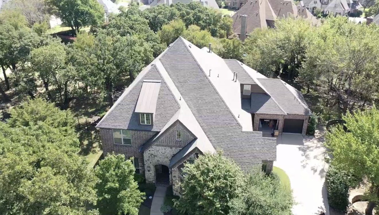 Vista con dron de una casa grande con un techo complicado en un lote con árboles