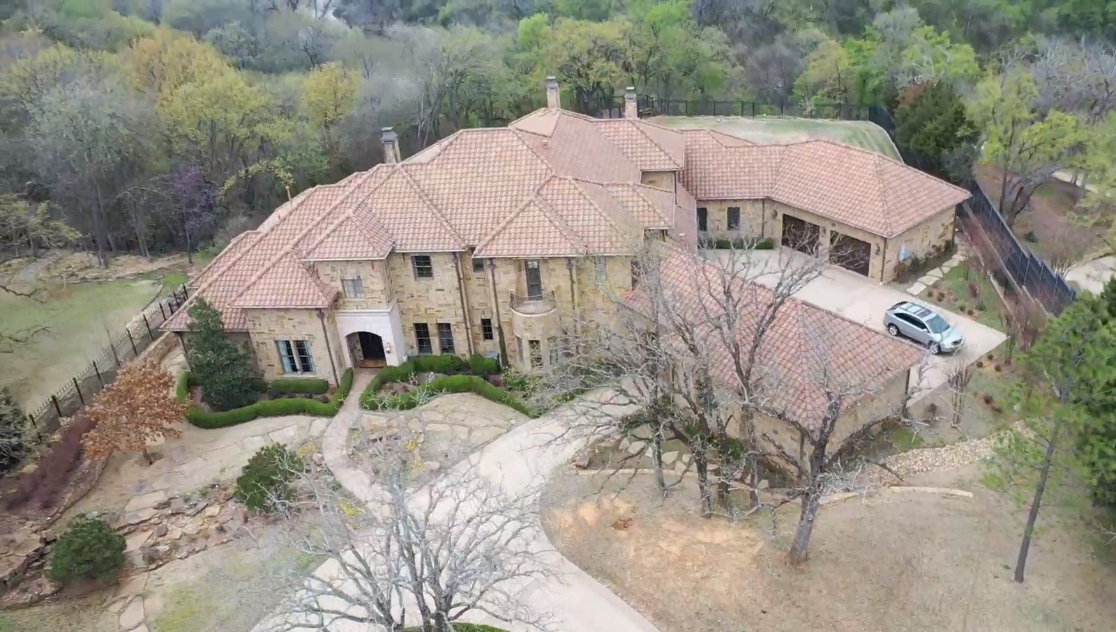 Vista con dron de una residencia de piedra con techo de teja de barro y una entrada de carro larga