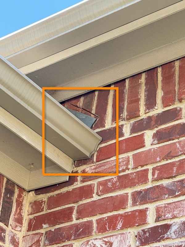 Unión de techo y pared donde una canaleta termina contra el ladrillo sin kick-out flashing, marcada en naranja