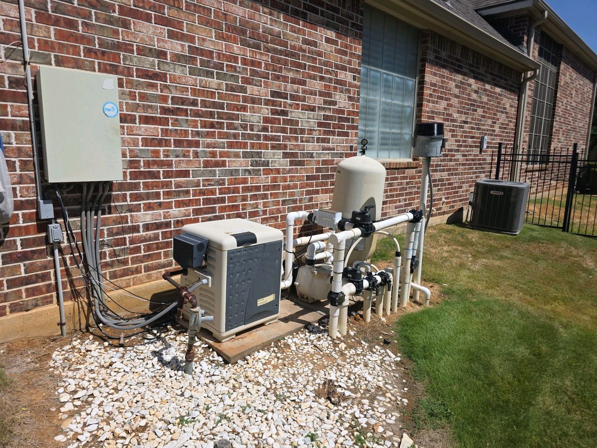 Pool equipment pad with heater, filter, pump, valves and control panel beside a brick house