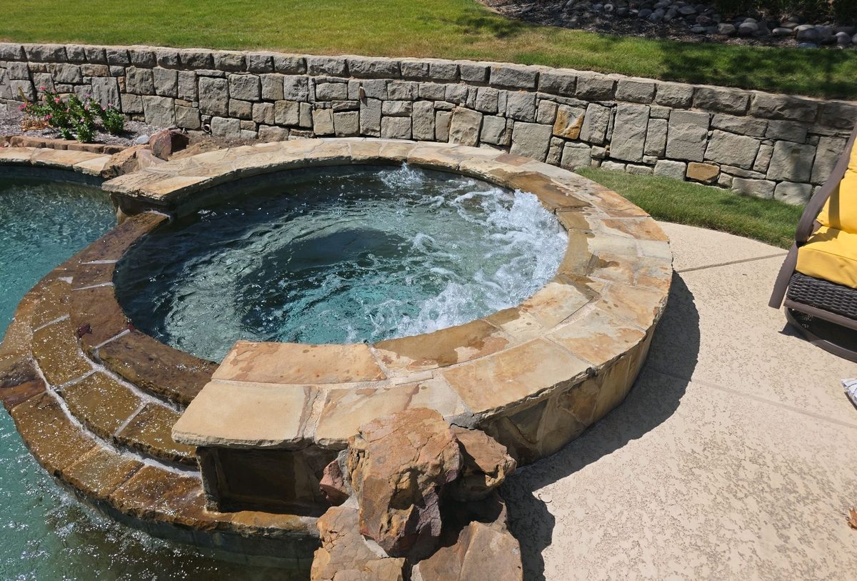 Stone spa with jets running beside a backyard pool