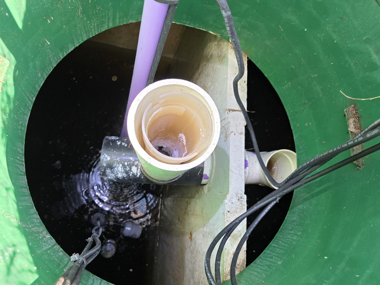 Interior de un tanque de bombeo séptico mostrando flotadores, tubería de la bomba y cableado