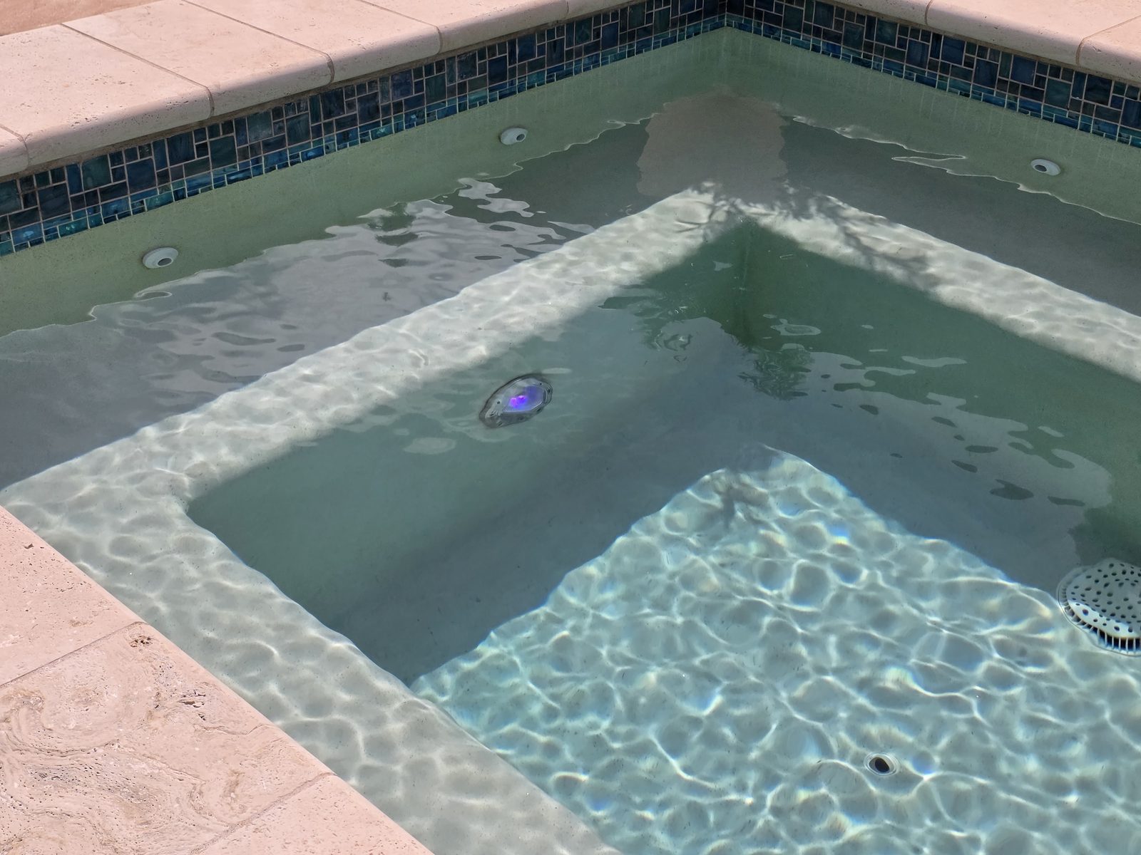 Interior del jacuzzi con asiento, franja de azulejo y luz subacuática