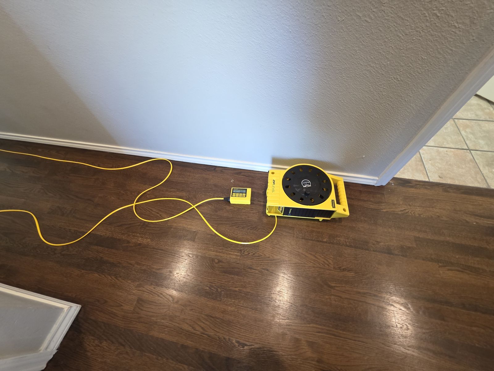 ZipLevel reference base set along a wall on dark hardwood with the yellow hose running to the readout