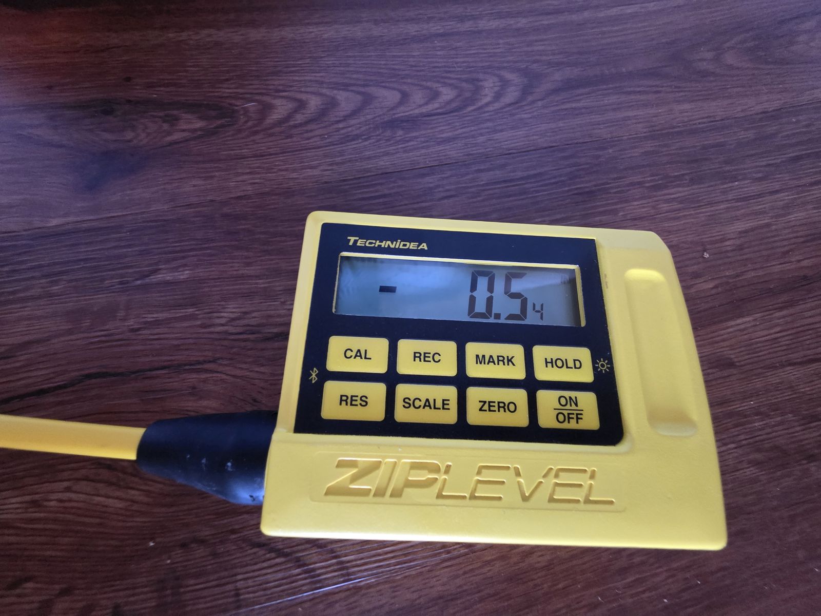 ZipLevel handheld readout showing -0.54 inches, a point lower than the reference, on a dark wood floor