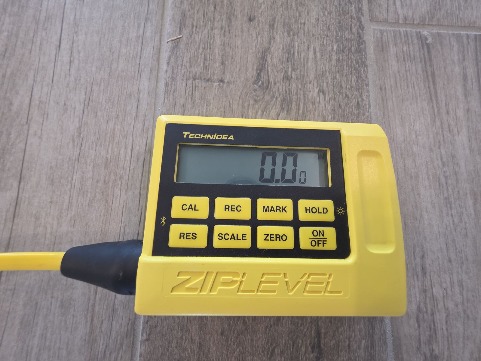 ZipLevel handheld readout showing 0.00 at a survey point on gray tile