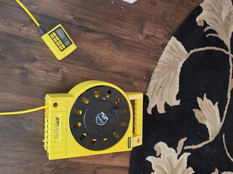 ZIPLEVEL reference base reel and handheld readout connected by a yellow cord on a wood floor